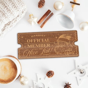 May include: A wooden ticket with the text "Harriet Official Member of the Nice List! Santa Claus" in gold lettering. The ticket is brown and has a distressed look.