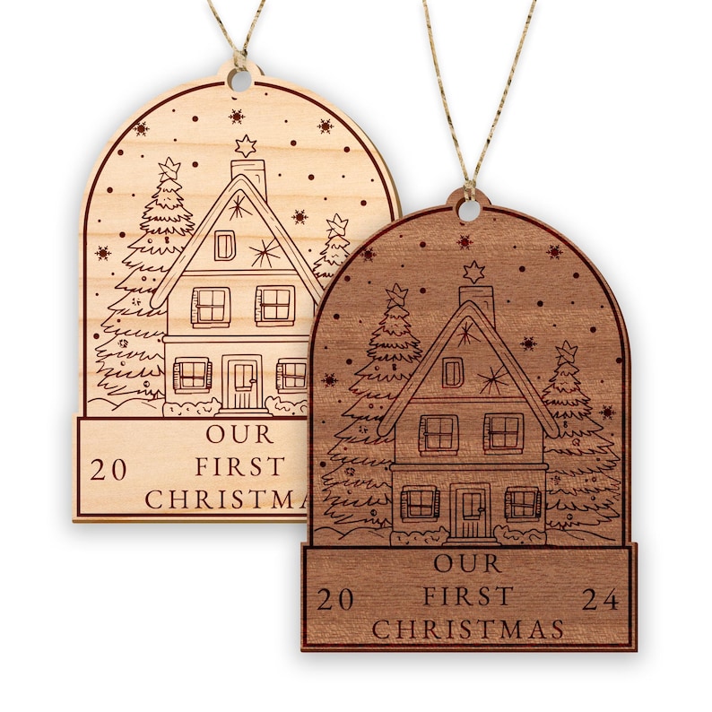 May include: Two wooden Christmas ornaments with a house and trees design. The ornaments are engraved with "Our First Christmas" and the years "20" and "24".