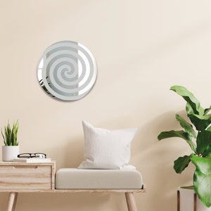 May include: A round mirror with a white spiral design on a light beige wall. The mirror is hanging above a light brown bench with a white pillow.