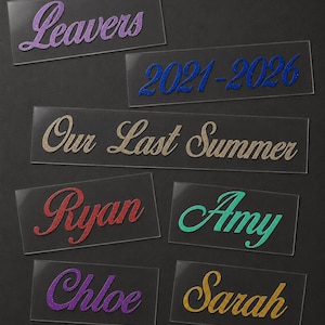 May include: Rectangular clear acrylic name tags with glitter lettering. The tags display the words "Leavers", "2021-2026", "Our Last Summer", "Ryan", "Amy", "Chloe", and "Sarah" in various colors including purple, blue, gold, red, and teal.