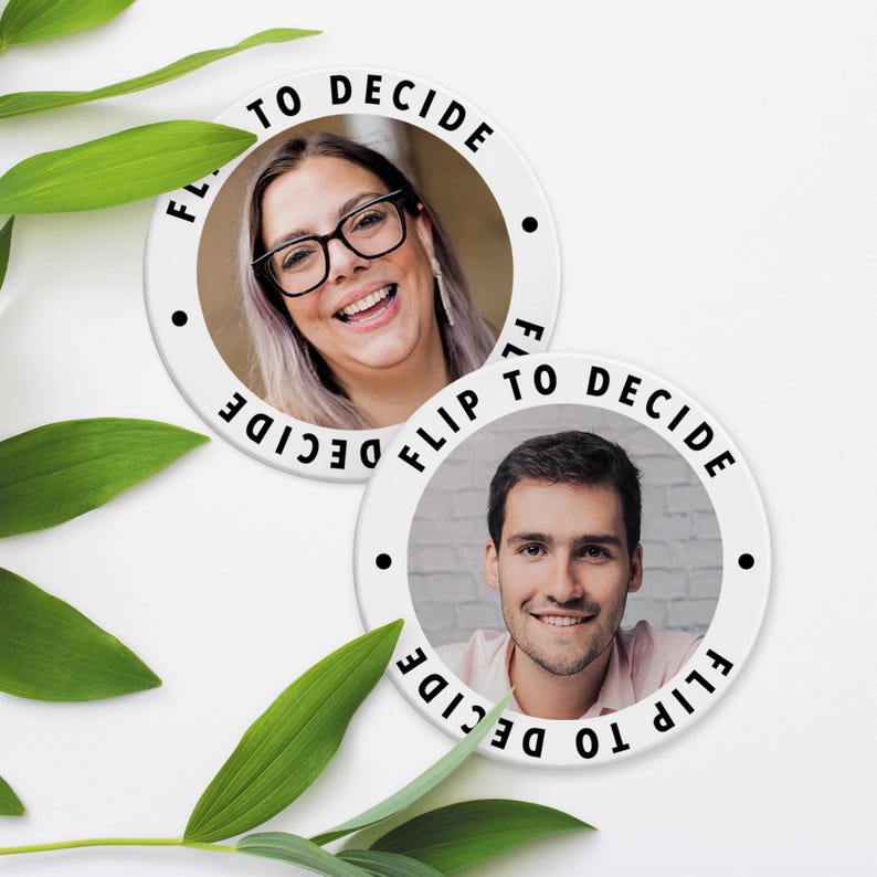 May include: Two white circular buttons with the text "FLIP TO DECIDE" around the edge. Each button features a smiling person's face in the center. The buttons are surrounded by green leaves.