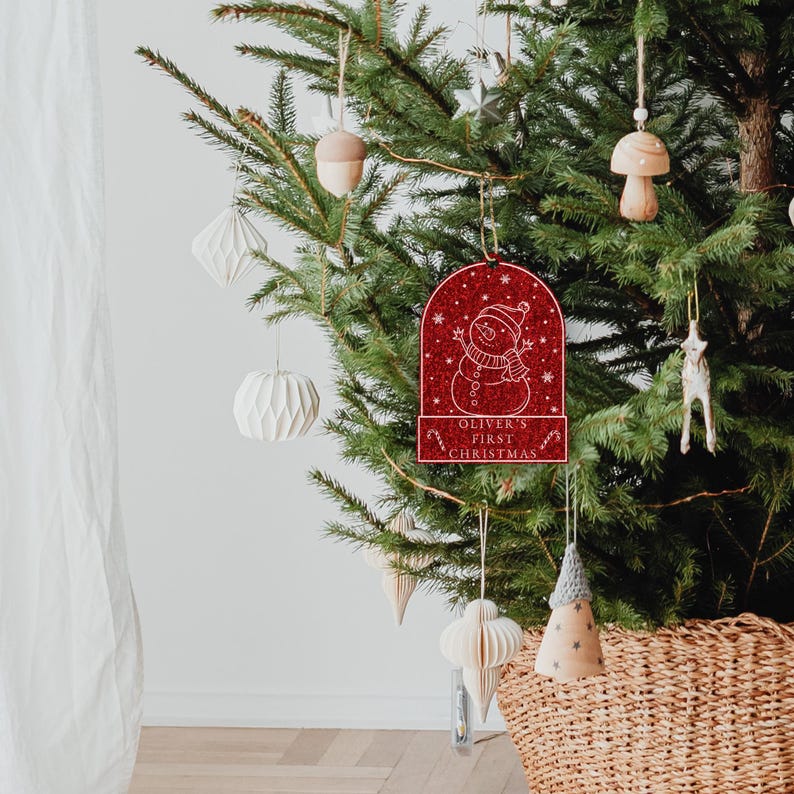 May include: Red glitter Christmas ornament with a snowman design and the text "Oliver's First Christmas".