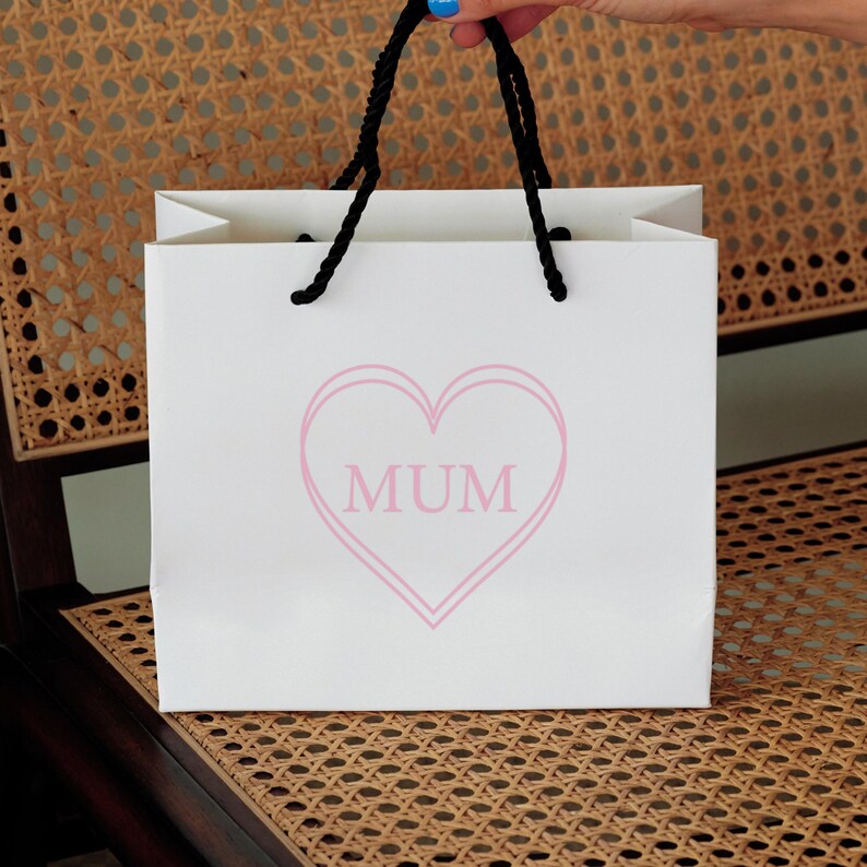 May include: White gift bag with black handles and a pink heart with the word "MUM" inside.