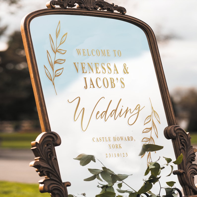 Pode incluir: Espelho dourado com um an&uacute;ncio de casamento. O an&uacute;ncio diz "Bem-vindos a Vanessa & Jacob's Wedding, Castle Howard, York, 23/10/23".