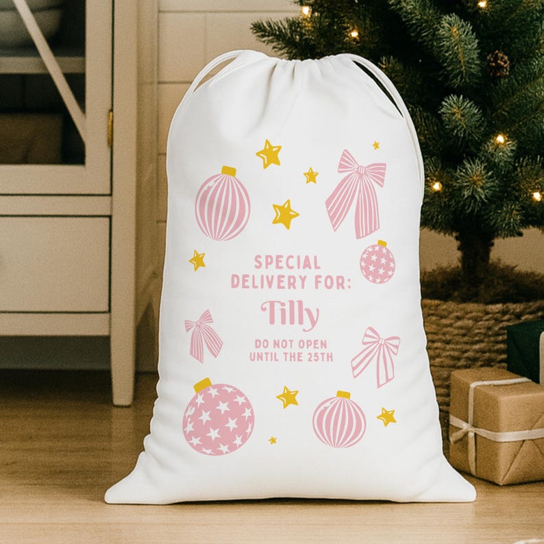 Puede incluir: Saco de regalo navide&ntilde;o blanco con cierre de cord&oacute;n. El saco est&aacute; decorado con adornos, lazos y estrellas rosas. El texto dice: "Special Delivery For: Tilly" y "Do Not Open Until The 25th".