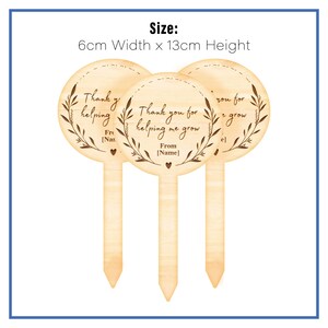 May include: Three wooden plant markers with a circular design. Each marker has a different message: "Thank you for helping me grow", "Thank y helping", and "Thank you for grow". Each marker has a small heart at the bottom and the text "From [Name]" on the middle marker.
