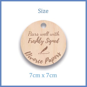 K&ouml;nnte beinhalten: Rundes Holzschild mit einem Loch oben. Das Schild hat einen Durchmesser von 7 cm und lautet "Pairs well with Freshly Signed Divorce Papers" mit einer Feder- und Tintenfassgrafik.