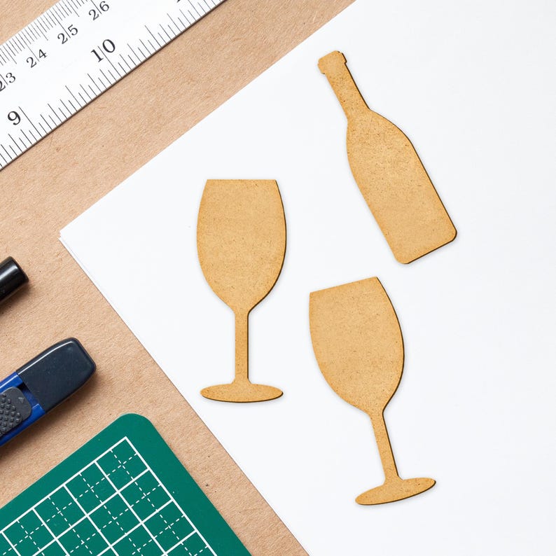 Puede incluir: Tres formas artesanales de madera: una botella de vino y dos copas de vino. Las formas son de color marr&oacute;n claro y tienen una textura rugosa y sin terminar.