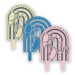 May include: Three cake toppers shaped like rainbows with the words "Oh Baby" in a script font. The rainbows are in yellow, blue, and pink.