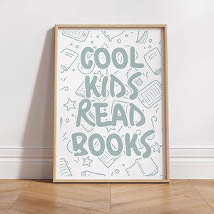 May include: A framed print with the text "COOL KIDS READ BOOKS" in light blue. The background features light blue illustrations of books, tablets, and stars. The frame is a light wood color, and the print is displayed on a wooden floor.