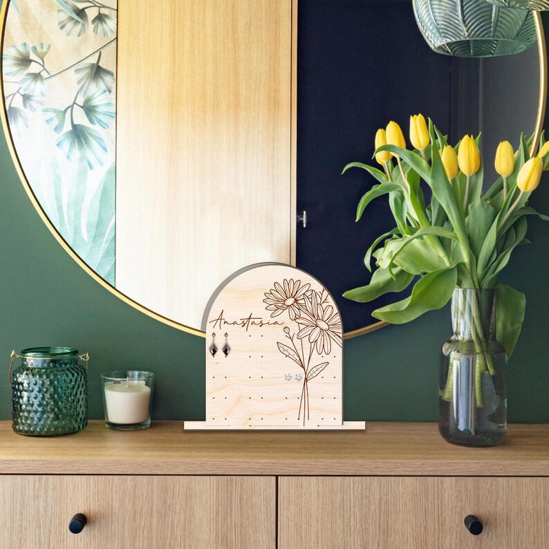 May include: Wooden earring holder with a floral design and the name Anastasia engraved on it. The holder has multiple holes for earrings and is displayed on a wooden surface.