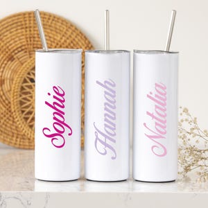 May include: Three white stainless steel tumblers with lids and straws. The tumblers have the names "Sophie", "Hannah", and "Natalia" written on them in pink, purple, and light pink lettering.