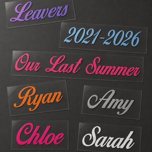 May include: A collection of clear acrylic name tags and labels with various text in different colors. The labels include the words "Leavers", "2021-2026", "Our Last Summer", "Ryan", "Amy", "Chloe", and "Sarah". The text is in a cursive font.