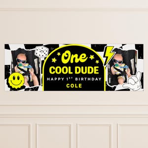 May include: A personalized banner with a black and white checkered pattern, featuring a baby in sunglasses and the text "One COOL DUDE HAPPY 1ST BIRTHDAY COLE." Includes a smiley face, dice, and a hand gesture.