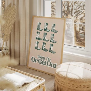 May include: A beige poster with a brown wooden frame features a grid of green cowboy boots with floral patterns. The text "Giddy Up Or Get Out" is printed in bold, green letters at the bottom of the poster.