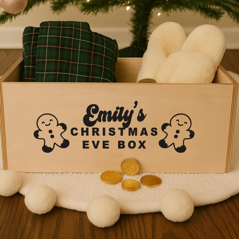 May include: A wooden Christmas Eve box with the text "Emily's CHRISTMAS EVE BOX" and gingerbread man graphics. The box contains a green plaid blanket, cream-coloured slippers, and gold-coloured coins. White pom-poms are in the foreground.