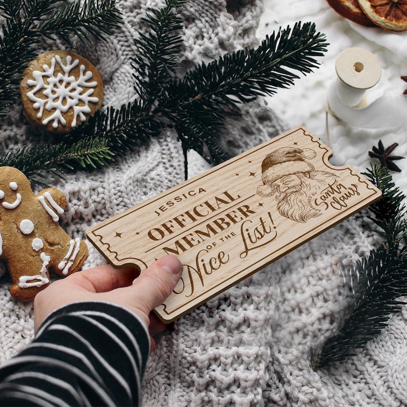 May include: A wooden ticket with the text "Jessica Official Member of the Nice List!" and a drawing of Santa Claus. The ticket is brown and has a distressed look.