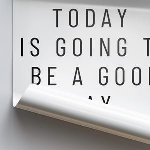 K&ouml;nnte beinhalten: Wei&szlig;es Poster mit schwarzem Text: &bdquo;TODAY IS GOING TO BE A GOOD DAY&ldquo;. Die untere rechte Ecke ist eingerollt und zeigt eine wei&szlig;e Oberfl&auml;che. Grauer Hintergrund.
