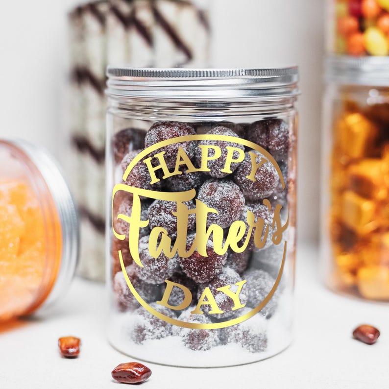 Puede incluir: Un tarro de vidrio transparente lleno de caramelos de chocolate, con una pegatina dorada que dice "Feliz D&iacute;a del Padre".