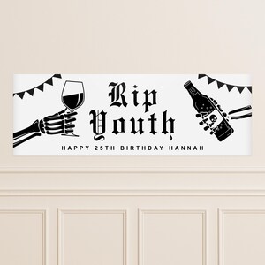 May include: A white banner with black graphics and text. The banner reads "Rip Youth" in gothic font, with "Happy 25th Birthday Hannah" below. A skeleton hand holds a wine glass, and another holds a bottle.