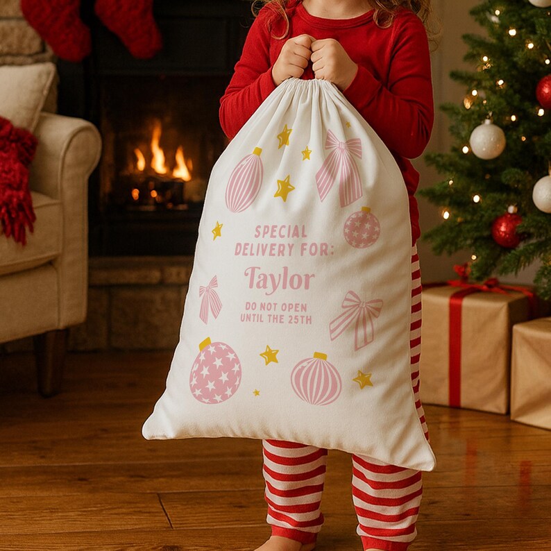 Puede incluir: Una gran bolsa de regalo navide&ntilde;a blanca con adornos, lazos y estrellas rosas. El texto "SPECIAL DELIVERY FOR: Taylor DO NOT OPEN UNTIL THE 25TH" est&aacute; impreso en la bolsa. La bolsa es sostenida por una persona con pijama rojo.