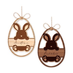 May include: Two wooden Easter egg ornaments with bunny silhouettes and personalized names. The ornament on the left is light brown with the name "Anastasia" and the ornament on the right is dark brown with the name "Nicholas".