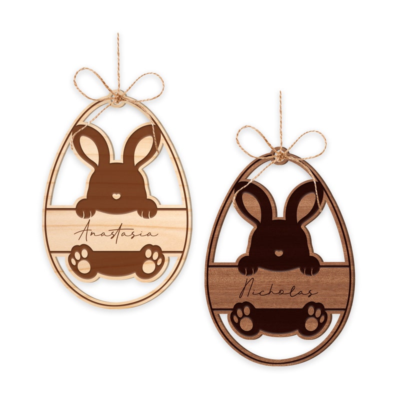 May include: Two wooden Easter egg ornaments with bunny silhouettes and personalized names. The ornament on the left is light brown with the name "Anastasia" and the ornament on the right is dark brown with the name "Nicholas".