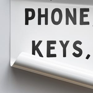 May include: White sign with black text that reads "PHONE, KEYS."