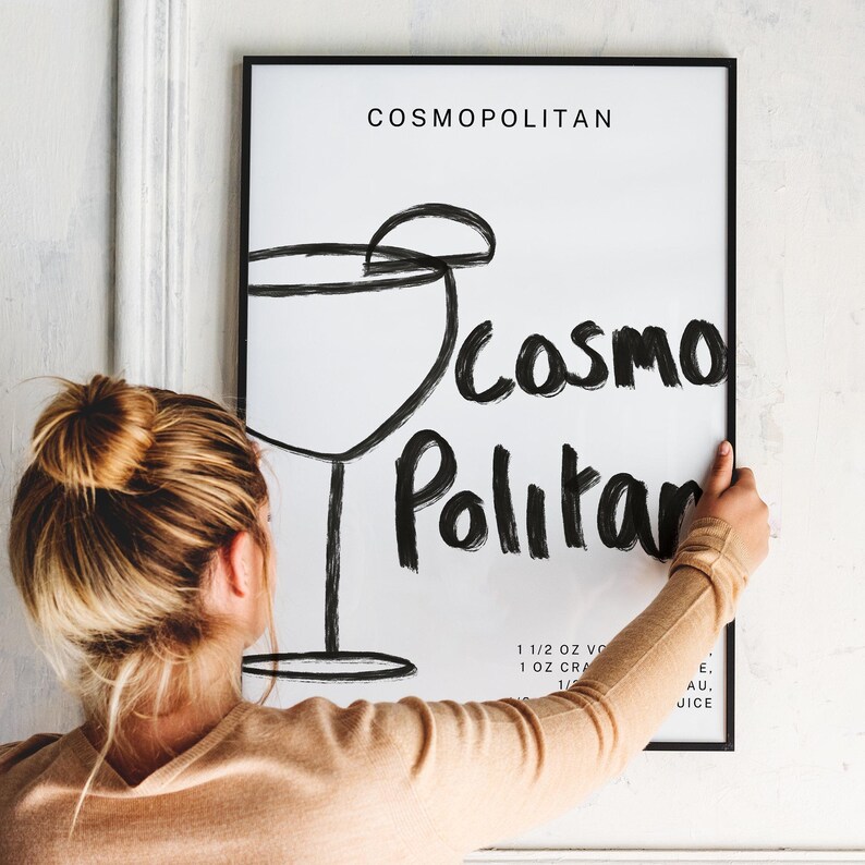 May include: A black and white illustration of a cocktail glass with the text "COSMOPOLITAN" and "COSMO Politan" written in a stylized font. The text below the illustration includes the ingredients for the cocktail: 1 1/2 oz vodka, 1 oz cranberry juice, 1/2 oz lime juice, and 1/4 oz Cointreau.