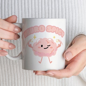 Puede incluir: Taza de cer&aacute;mica blanca con un personaje de dibujos animados de cerebro rosa flexionando los brazos y el texto "Neuro Spicy" en letras rosas.