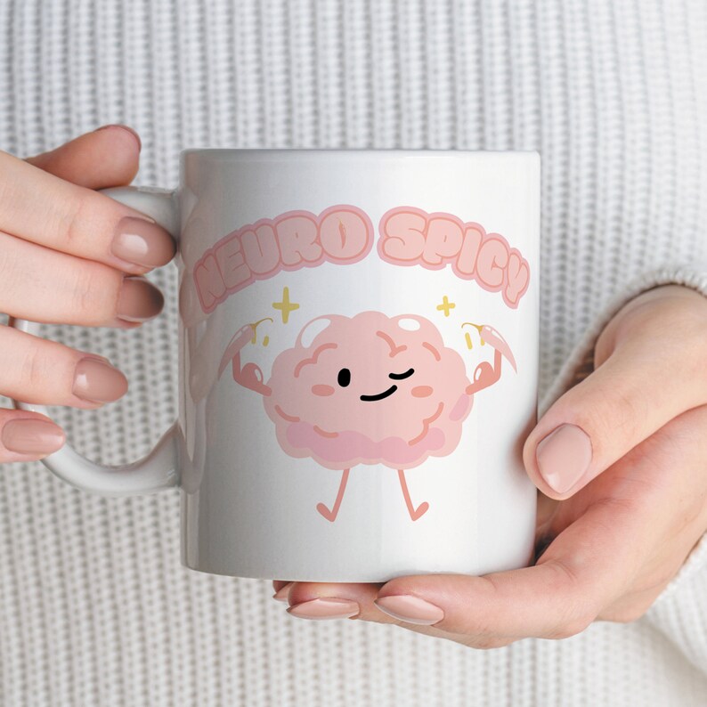 Puede incluir: Taza de cer&aacute;mica blanca con un personaje de dibujos animados de cerebro rosa flexionando los brazos y el texto "Neuro Spicy" en letras rosas.
