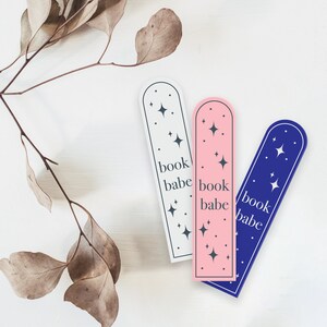 May include: Three bookmark designs with a star pattern and the text "book babe". The bookmarks are white, pink, and blue.