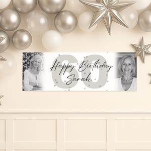 May include: A banner with the text "Happy Birthday Sarah" and the number "60" in gray. The banner has two black and white photos of a woman. Silver balloons and star decorations are in the background.