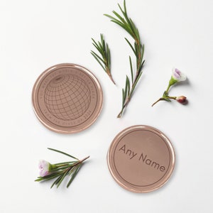 May include: Two rose gold colored round metal tokens. One token has the text "You make the world a better place from the class of 2024" and a globe graphic. The other token has the text "Any Name".