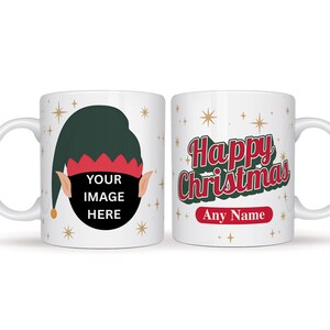 May include: White ceramic Christmas mug. One side has an elf graphic with the text "YOUR IMAGE HERE". The other side displays "Happy Christmas" in red and green, with space for a name. Festive design with star accents.