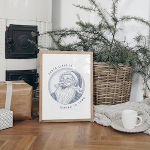May include: A framed print with a white background and a blue illustration of Santa Claus with the text "Santa Claus is coming to town".