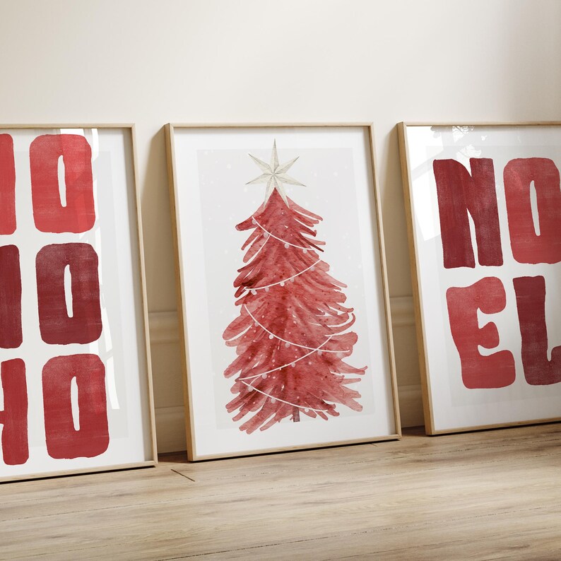Puede incluir: Tres impresiones art&iacute;sticas enmarcadas con tem&aacute;tica navide&ntilde;a. La impresi&oacute;n central presenta un &aacute;rbol de Navidad rojo en acuarela con una estrella y luces de cadena. Las otras dos impresiones tienen las palabras "NO" y "HO HO" en letras rojas.