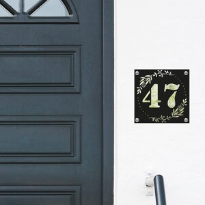 May include: Black house number sign with a white floral design and the number 47 in white.