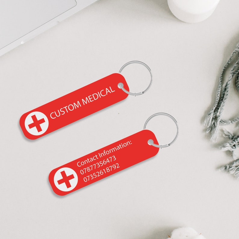 May include: Two red keychains with a white plus sign and white text. The first keychain says "CUSTOM MEDICAL". The second keychain says "Contact Information: 07877356473 07352618792".