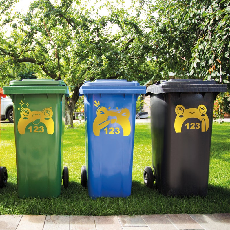 Puede incluir: Tres contenedores de reciclaje con pegatinas de ranas. Los contenedores son verdes, azules y negros. Cada contenedor tiene una pegatina de rana con el n&uacute;mero 123.