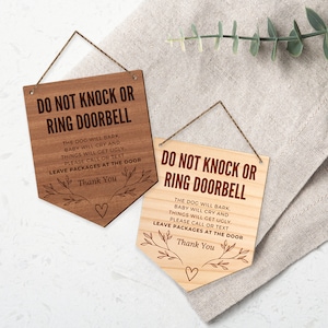 May include: Two wooden signs with a rustic brown finish and a rope hanger. The signs are shaped like a pennant and have the text "Do Not Knock or Ring Doorbell" in red. The text below the main text reads "The dog will bark, baby will cry and things will get ugly. Please call or text. Leave packages at the door. Thank you."