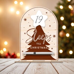 Puede incluir: Un letrero de cuenta atr&aacute;s de Navidad de madera con una estrella blanca y el n&uacute;mero 19 en &eacute;l. El letrero dice "Sleeps till Christmas" y tiene un marcador de borrado en seco blanco.