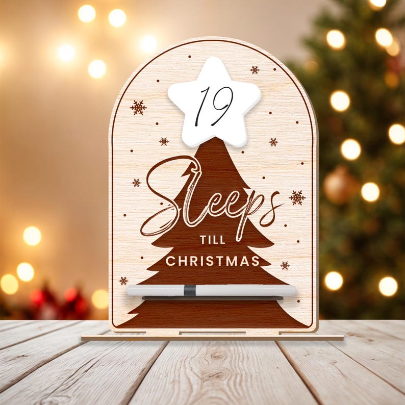 Puede incluir: Un letrero de cuenta atr&aacute;s de Navidad de madera con una estrella blanca y el n&uacute;mero 19 en &eacute;l. El letrero dice "Sleeps till Christmas" y tiene un marcador de borrado en seco blanco.