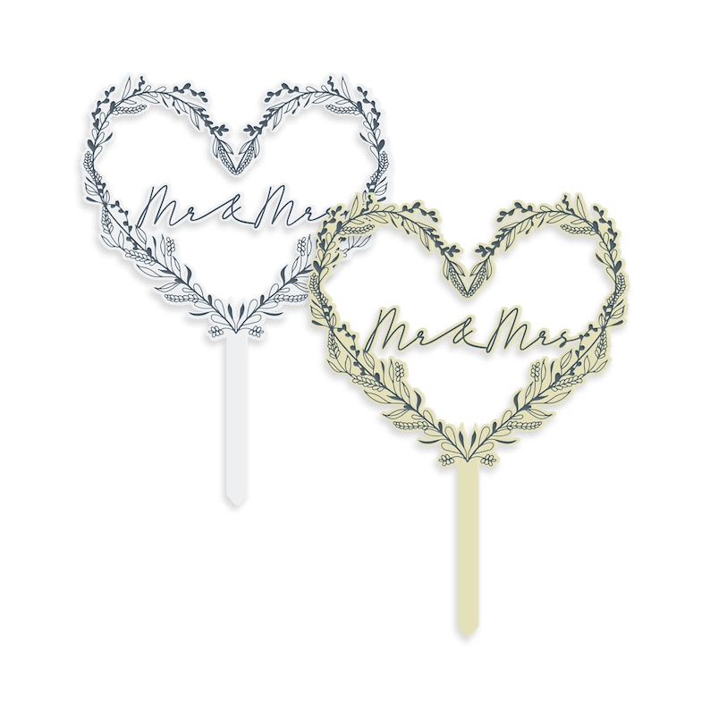 May include: Two heart-shaped cake toppers with floral wreaths and the text "Mr & Mrs" in a cursive font. One topper is white with a white stick, and the other is beige with a beige stick.