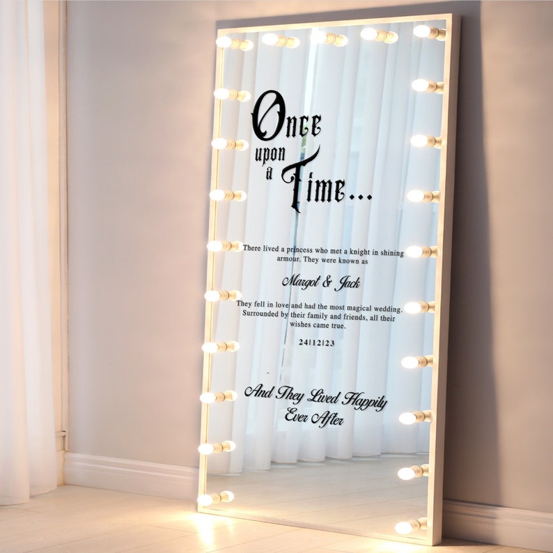 May include: A white vanity mirror with a large, rectangular mirror and a white frame. The mirror has a decorative sticker with the text "Once upon a Time..." and a wedding-themed message. The mirror has a row of light bulbs around the perimeter.