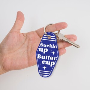 May include: Blue motel key chain with the text "Buckle up Butter cup" in white. The keychain has a silver key ring.