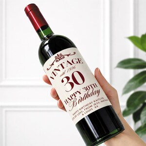 May include: A wine bottle with a red cap and a label that reads "VINTAGE estd 1996 30 HAPPY 30TH Birthday." The label also includes the text "HAPPY BIRTHDAY KAITLYN OTS OF LOVE, FROM JESS, NATHAN & LOUIS XX."