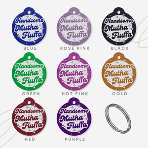 Op de afbeelding: Negen ronde huisdier-hangers in verschillende kleuren, elk met de tekst "Handsome Mutha Fluffa" in een wit retro-lettertype met witte sterren rond de tekst. De hangers zijn blauw, roze, zwart, groen, roze, goud, rood, paars en zilver.