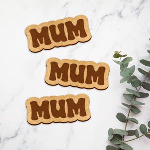 May include: Three brown wooden coasters with the word "MUM" in a retro font.