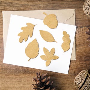 May include: A set of six brown paper cutouts of leaves and an acorn on a white background. The cutouts are arranged in a semi-circle.